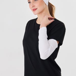 Può includere: Una donna indossa una fascia bianca, una maglietta nera e maniche bianche. La donna indossa anche una gonna con stampa leopardata. Lo sfondo è bianco.