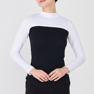 May include: A two-tone long-sleeved top with a white upper section and black lower section. The top has a high neckline and is paired with black pants and a black head covering. The outfit is simple and elegant.