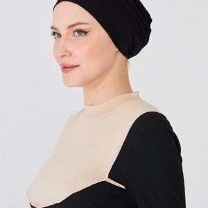 May include: A black head covering and a two-tone top. The top has a beige upper section and black long sleeves. The head covering is a solid black color. The outfit is simple and elegant.
