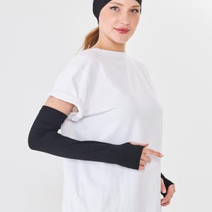 May include: A person wearing a black headband, white t-shirt, and black fingerless sleeves. The sleeves cover the arms from the wrist to the upper arm. The headband is wide and covers the forehead.