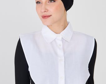 May include: A white collared shirt with a black long-sleeved top. The shirt has a classic button-down design. A black head covering is also visible.
