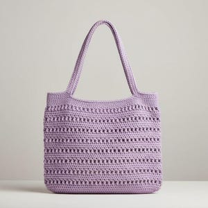 Puede incluir: Un bolso tote de crochet lavanda con dos asas. El bolso tiene forma rectangular con un diseño texturizado y calado. Las asas son lo suficientemente largas para llevarlo al hombro. El bolso está hecho de un material suave y duradero.