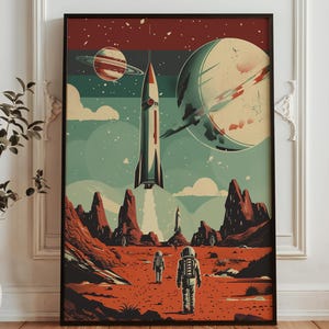 May include: Framed retro space travel art print. The artwork depicts a rocket launching, astronauts on a red planet, and planets in the background. The colour scheme includes red, teal, and cream.