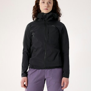 May include: A black hooded jacket with a front zipper and a small chest pocket. The jacket is paired with purple pants. The model is standing in front of a white background.