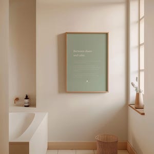 Może przedstawiać: Prostokątny plakat ścienny w jasnej drewnianej ramie z szałwiowo-zielonym tłem, zawierający biały napis "Between chaos and calm.", mniejszy, mniej czytelny biały tekst oraz małą okrągłą ikonę umieszczoną na dole.