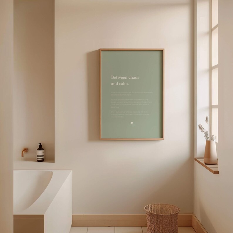 Może przedstawiać: Prostokątny plakat ścienny w jasnej drewnianej ramie z szałwiowo-zielonym tłem, zawierający biały napis "Between chaos and calm.", mniejszy, mniej czytelny biały tekst oraz małą okrągłą ikonę umieszczoną na dole.