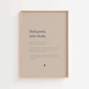 May include: A rectangular wall art print in a light wood frame featuring a beige background with dark blue text. The text reads: Held gently, held wholly. Gentle doesn't mean fragile. Wholly doesn't mean fixed. This is the paradox of healing.