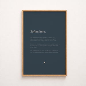 May include: A rectangular wall art print in a light wood frame featuring a dark blue background with white text that reads: Soften here. The armour you've been wearing is heavy. The vigilance is exhausting. The constant bracing for impact takes more energy than the impact itself. Soften here. Not because the world is suddenly safe, but because you need rest from being so ready for it not to be. This space holds you while you let your guard down. You can release the clench. You're allowed to exhale.