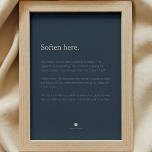 May include: A rectangular light wood frame containing a dark blue print with the white text: Soften here. The armour you've been wearing is heavy. The vigilance is exhausting. The constant bracing for impact takes more energy than the impact itself.