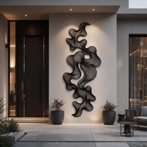 Può includere: Una grande scultura da parete nera verticale caratterizzata da una serie di linee ondulate, fluide e interconnesse che creano un motivo organico astratto. L'oggetto è montato su una parete esterna chiara tra due piante in vaso grigio scuro.