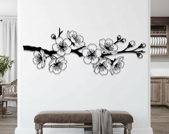 Könnte beinhalten: Schwarze Metall-Wandkunst, die einen Kirschblütenzweig mit detaillierten Blüten und Knospen darstellt. Das Kunstwerk ist an einer weißen Wand über einer Bank mit einer grauen Decke angebracht. Das Design verleiht eine Note von naturnaher Dekoration.