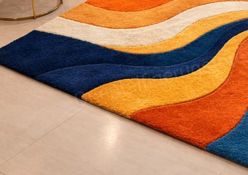 May include: A vibrant area rug with a flowing, wave-like pattern. The rug showcases bands of orange, yellow, white, and navy blue. The rug has a soft, textured feel and is placed on a light-coloured tiled floor.