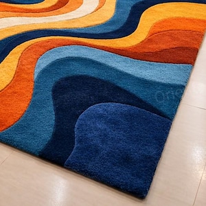 May include: A patterned rug with a wave-like design in shades of orange, yellow, white, and blue. The rug's design creates a sense of movement and adds a modern touch to any space. The rug is a statement piece.