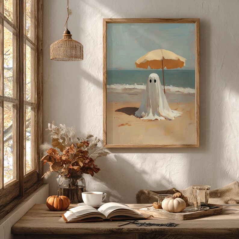 May include: A framed wall art print depicting a white ghost figure standing on a sandy beach under a yellow beach umbrella, with the ocean and sky in the background. The artwork features a painted style with visible brushstrokes and soft colors.