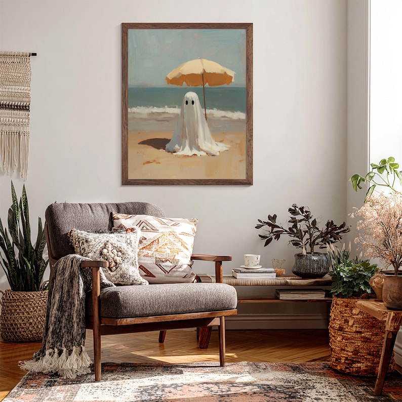 May include: A framed wall art print featuring a white ghost figure standing on a sandy beach under a yellow beach umbrella. The scene depicts the ocean waves in the background with a clear sky. The artwork is enclosed in a dark brown wooden frame.