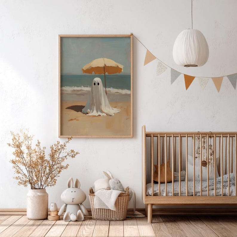 May include: A rectangular wall art print featuring a painting of a white ghost standing on a sandy beach under a tan umbrella, with the ocean and sky in the background. The artwork is displayed in a light wood frame hanging on a white wall.