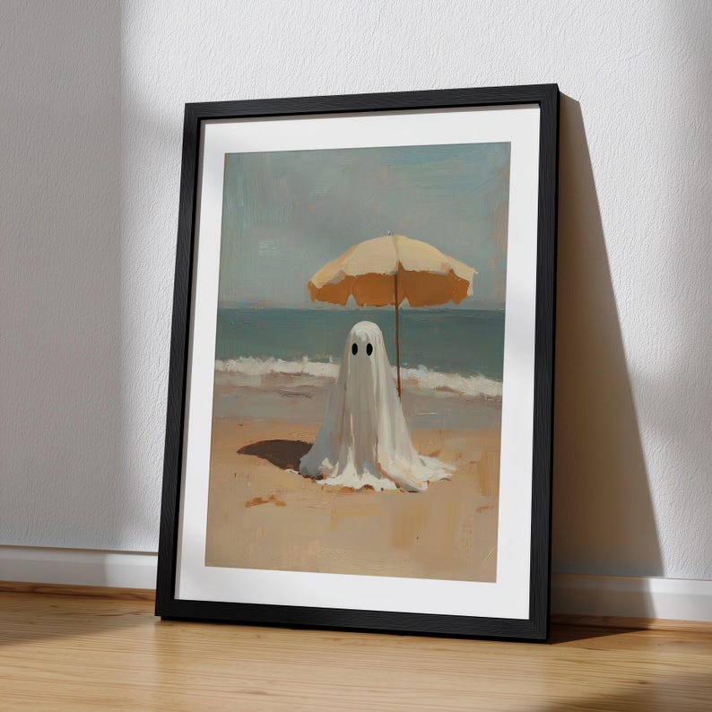May include: A framed wall art print featuring a painting of a white ghost figure standing on a sandy beach under a yellow beach umbrella. The scene depicts the ocean waves in the background with a soft, painterly texture and muted color palette.