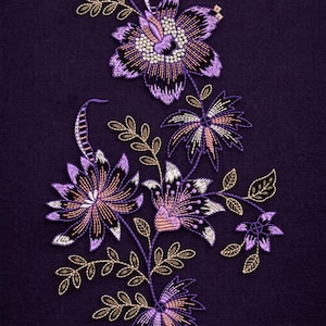 Pode incluir: Close-up de um tecido roxo escuro com um design floral bordado. O bordado apresenta fios roxos, pretos, brancos e dourados, criando flores e folhas detalhadas. O design é intrincado e decorativo.