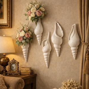 Pode incluir: Vasos de parede de cerâmica branca em forma de concha, cada um com um design único, montados numa parede bege. Dois vasos contêm buquês de rosas cor-de-rosa e brancas. O quarto é decorado com uma lâmpada, um relógio e uma cesta de conchas.