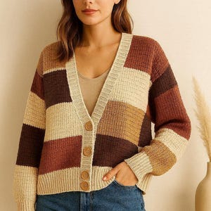 Può includere: Un cardigan multicolore con scollo a V e chiusura con bottoni. Il maglione presenta un design patchwork nei toni del marrone, beige e marrone chiaro. La modella indossa jeans blu. Questo accogliente capo in maglia è perfetto per l'autunno.