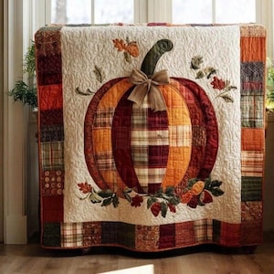 May include: A quilted pumpkin design, featuring a large pumpkin with a plaid pattern in shades of orange, red, and brown. The pumpkin is adorned with a bow and surrounded by leaves and berries. The quilt has a cream background and a patchwork border.