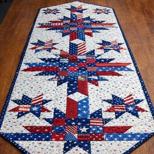 May include: A patriotic table runner featuring a patchwork design with red, white, and blue stars and stripes. The runner is rectangular, with a central design of stars and stripes, and measures approximately 40 inches long.