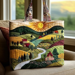 May include: Quilted tote bag featuring a vibrant landscape scene. The design includes rolling hills, a bright yellow sun, houses, trees, and a winding road. The bag has patterned handles and is made of various fabrics.