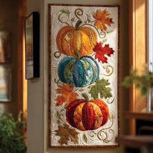 May include: A quilted wall hanging featuring three pumpkins in shades of orange, blue, and red. The pumpkins are surrounded by autumn leaves in various colors, with embroidered vines and a cream-colored background. The artwork is rectangular and has a decorative border.