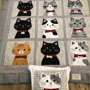 May include: A quilted blanket featuring a grid of cat portraits in various colors and patterns, each wearing a red bow tie, alongside a matching square pillow with a cat illustration and the name Arlo embroidered in black thread.
