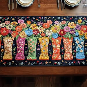 May include: A quilted table runner featuring a vibrant floral design with seven colorful rain boots. The boots are filled with various floral patterns and sit beneath a row of colorful flowers. The runner is on a dark blue background.