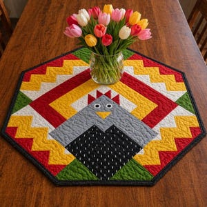 May include: A colorful, quilted table runner with a geometric design and a central chicken motif. The runner features red, yellow, green, white, and black accents. A glass vase holds a bouquet of tulips in various colors.