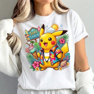 May include: White t-shirt featuring a cartoon Pikachu character in a Hawaiian shirt, holding an ice cream cone. The design includes a "Surf Shack" sign, tropical flowers, and a sun.
