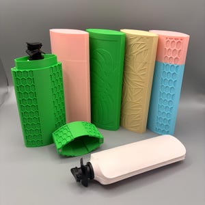 Könnte beinhalten: Eine Sammlung farbenfroher, 3D-gedruckter Flaschenverschlüsse und -hüllen. Die Verschlüsse sind schwarz und weiß, während die Hüllen in verschiedenen Farben erhältlich sind, darunter Grün, Rosa, Gelb und Blau. Einige Hüllen haben strukturierte Designs.
