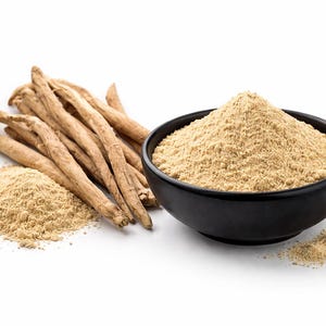 May include: An image of ashwagandha, a herbal supplement. It features dried ashwagandha roots, a pile of ashwagandha powder, and a black bowl filled with ashwagandha powder. The powder is a light tan colour.