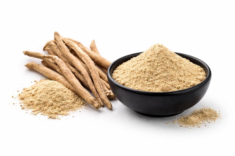 May include: An image of ashwagandha, a herbal supplement. It features dried ashwagandha roots, a pile of ashwagandha powder, and a black bowl filled with ashwagandha powder. The powder is a light tan colour.