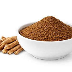 May include: A white ceramic bowl filled with brown powder, likely a spice or supplement, sits next to a small pile of tan, dried roots. The items are set against a clean white background.
