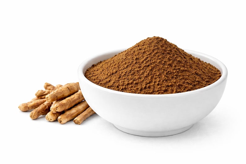 May include: A white ceramic bowl filled with brown powder, likely a spice or supplement, sits next to a small pile of tan, dried roots. The items are set against a clean white background.