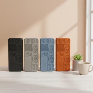 Peut inclure: Quatre étuis rectangulaires, noirs, gris, bleus et oranges, avec des motifs uniques, sont présentés sur une surface en bois clair. Les motifs comprennent des formes géométriques et un motif de main. Une petite plante succulente et une tasse sont également présentes.