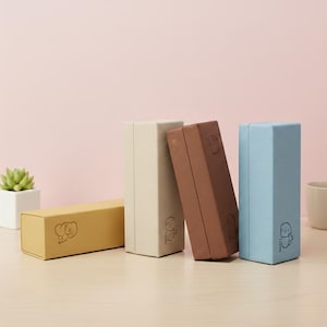 May include: Four rectangular boxes in yellow, cream, brown, and blue. Each box features a small cartoon character illustration and text. The boxes are arranged on a light surface with a pink backdrop.