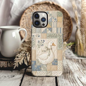May include: A smartphone case featuring a quilted patchwork design in soft blue, beige, and cream tones. The pattern includes small floral prints, gingham checks, and a central illustration of a white goose wearing a small patterned neck ribbon.
