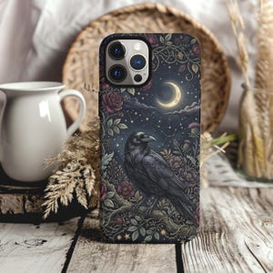 May include: A smartphone case featuring a dark, detailed illustration of a black raven perched on a branch. The design includes deep red roses, green foliage, a glowing crescent moon, and a starry night sky background with constellations.