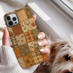 May include: A smartphone case featuring a patchwork design with various autumn-themed patterns including orange pumpkins, brown maple leaves, floral prints, and plaid squares in shades of olive green, mustard yellow, and burnt orange.