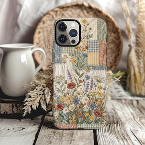 May include: A smartphone case featuring a quilted patchwork design with a variety of colorful wildflowers, including red poppies, blue cornflowers, and white daisies, layered over a background of soft pastel squares in gingham and floral patterns.