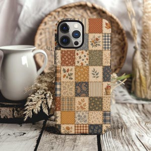 May include: A smartphone case featuring a patchwork design of various squares with autumn-inspired patterns, including floral prints, plaid, gingham, paisley, and small leaf motifs in shades of orange, brown, cream, blue, and green.