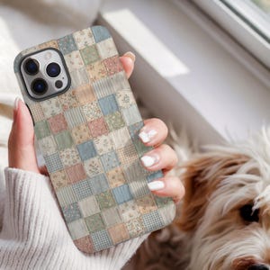 May include: A phone case with a patchwork design in pastel colors, including pink, blue, and beige squares with floral and gingham patterns. The case has a camera cutout and is held by a person.