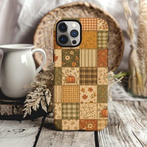 May include: A rectangular smartphone case featuring a patchwork design of autumn-themed squares. The pattern includes orange pumpkins, brown and green plaid, yellow gingham, and scattered maple leaves in shades of orange, brown, and cream.
