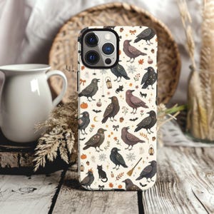 May include: A smartphone case featuring a cream-colored background with a repeating pattern of black crows, small black cats, orange pumpkins, spider webs, lanterns, acorns, bows, and tiny ghosts. The design includes various small stars and floral elements.
