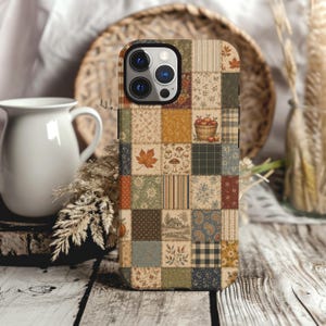 May include: A smartphone case featuring a patchwork design with various autumn-themed patterns including maple leaves, mushrooms, a basket of apples, plaid, floral prints, and a small house illustration in shades of brown, orange, green, and cream.