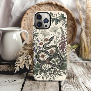 May include: A cream-coloured smartphone case featuring a detailed illustration of a coiled dark snake surrounded by botanical elements including purple foxgloves, blue bellflowers, small daisies, and green leafy vines on a light background.