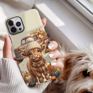 May include: A cream-colored smartphone case featuring a graphic illustration of a fluffy Highland cow wearing a beige knit beanie and a plaid scarf, surrounded by orange and black pumpkins and a vintage brown pickup truck on a light background.